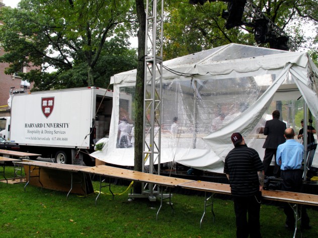 Photograph by Harvard Magazine/JC Workers assembled the cake under a tent to protect it from the rainy weather. A Harvard Dining Services truck brought over the individual sheet cakes, which form the 15-by-18-foot H-shaped cake. Sixty individual sheet cakes were baked, two per day, by Flour bakery and deep frozen at Harvard awaiting the day of the celebration.