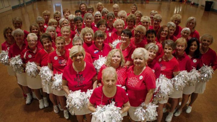 Photo of a cheerleader group composed of elderly women, all in red tops and white skirts, with pompoms