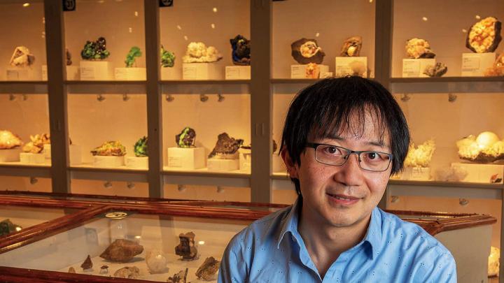 Roger Fu sits in front of a display case of rock samples
