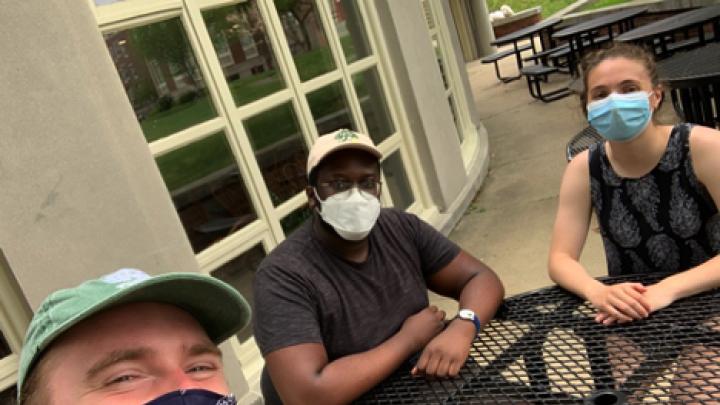 Photo of the author sitting with two friends, all in masks, in the Radcliffe Quadrangle as they watched virtual Commencement