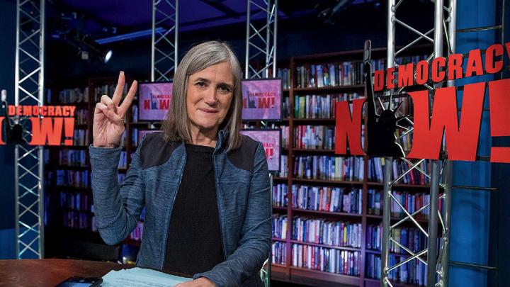 Amy Goodman featured in her broadcast studio giving the peace sign