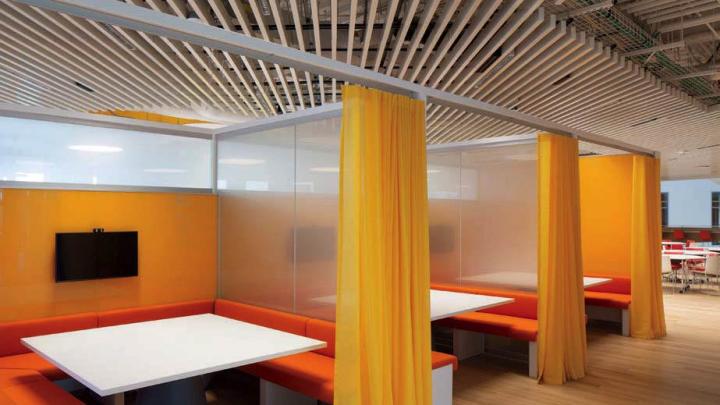 A centrally located 3,100-square-foot library has study carrels with orange benches, white desktops, and yellow privacy curtains.