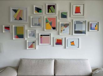 A collection of abstract geometric paintings hang above a white couch