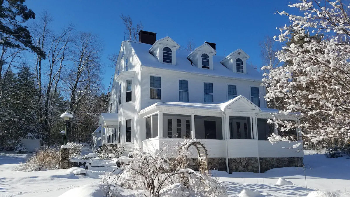 Large white 3 story house with snow on the house and the property. 