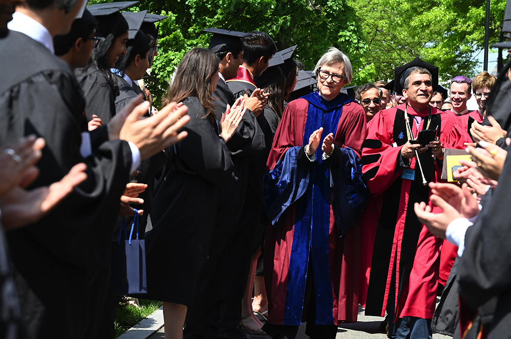 graduates in black caps and gowns cheer as Drew Gilpin Faust and Rakesh Khaurana walk between the student 