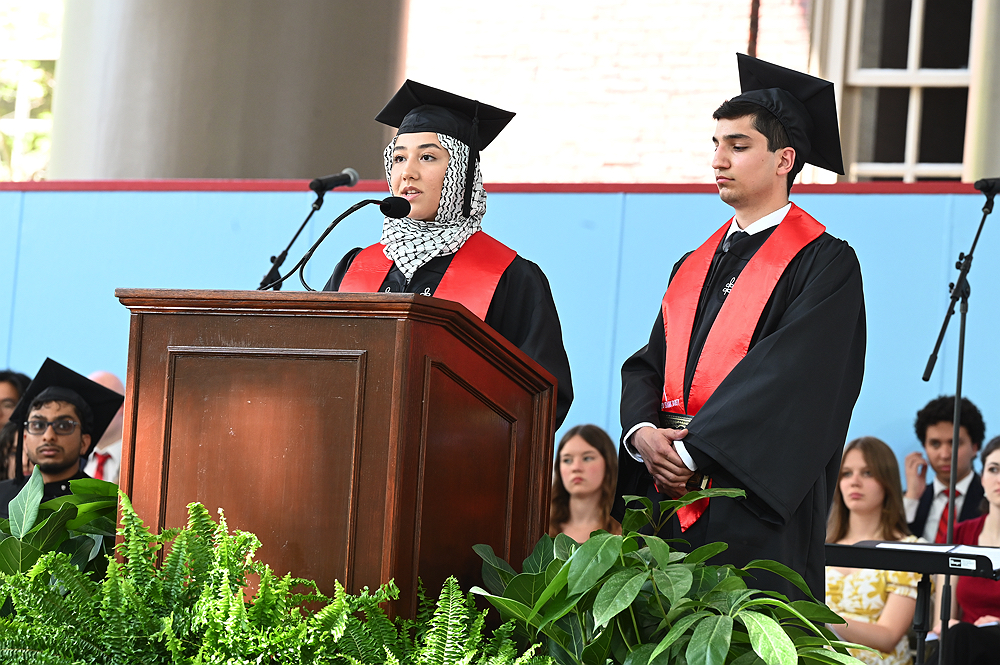 graduates at the podium wearing black caps and robes and red sashes