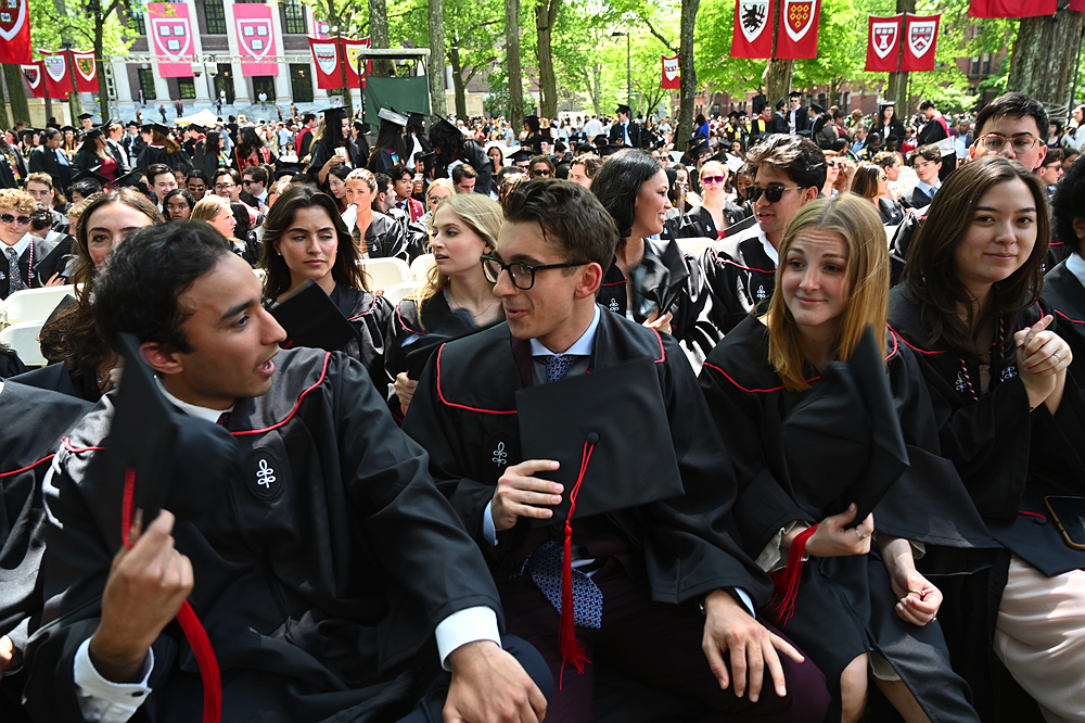 graduates wearing black robes fan themselves with their caps to keep cool in the heat