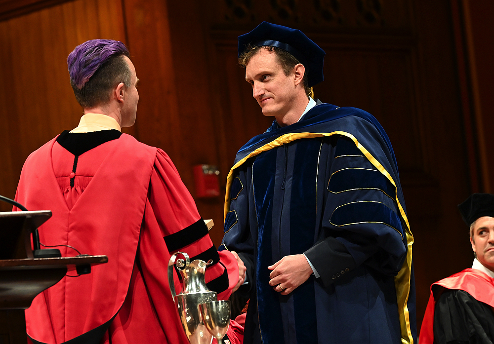 man in blue robe accepting prize from man in red robe
