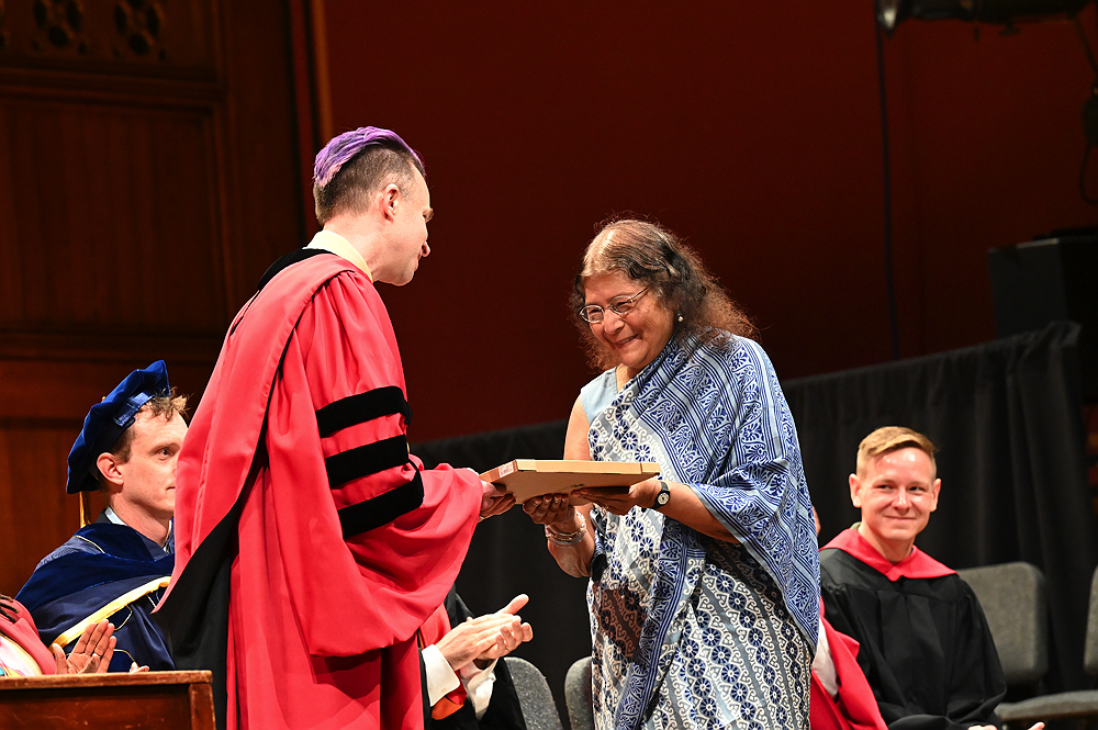 woman in blue and white sari accepting award from man in red robe