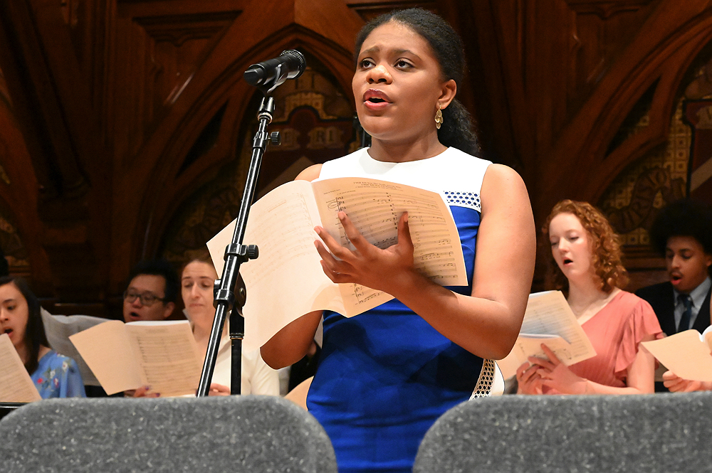 woman singing with chorus behind her in Sanders Theater