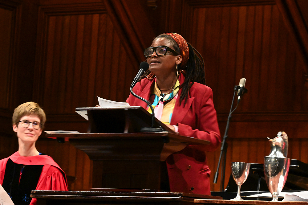 Tracy K. Smith, wearing a red suit, addresses the audience at Sanders Theater