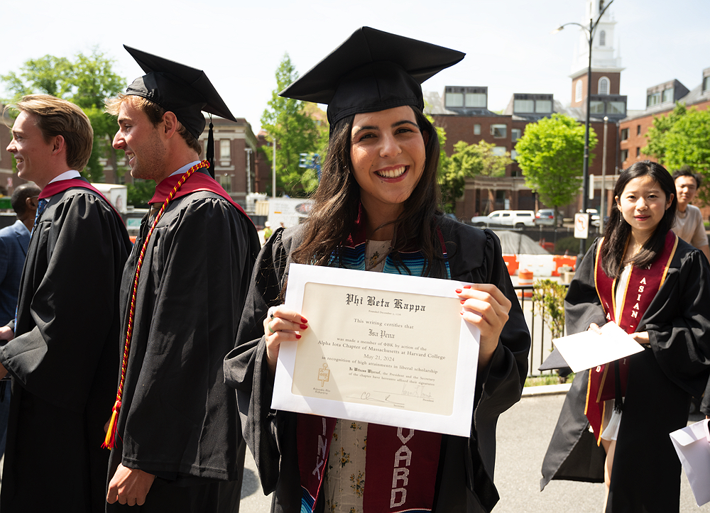 Graduate Isa Pena, wearing black cap and gown, shows off her Phi Beta Kappa diploma
