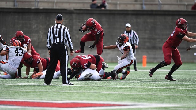 Harvard running back Aaron Shampklin hops over a Harvard teammate with a football in hand.