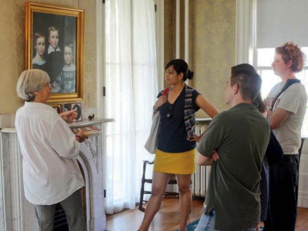 Museum visitors in the parlor view a group portrait of Dickinson and her brother and sister as children.