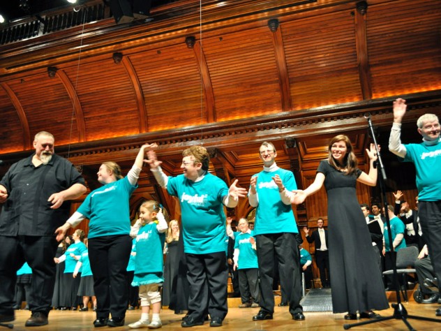 Courtesy of Marshall Kurtzman Local composer Nick Page (at left), conductor of the Mystic Chorale, takes a bow with chorus and Collegium Musicum members after they performed his song “Do You Shine” (written especially for Joyful Noise) as an encore. Sharing the applause is Katie Fromm, daughter of the chorus’s co-founder and conductor, Allison Fromm.