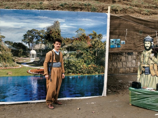 Photograph by Susan Meiselas/Magnum Photos A Peshmerga soldier poses for a formal portrait by a street photographer in Arbil, Northern Iraq, 1991. Family members carried portraits of Peshmerga martyrs in small lockets pinned to their clothes as a remembrance. —From the series <em>Kurdistan</em>