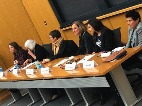 Six women sit at a table at the front of an auditorium.