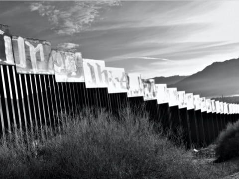 A photograph of the border wall stretching toward a mountain in the distance