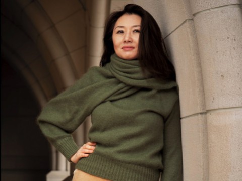 Portrait of Jeannie Suk Gersen, an elegantly dressed Korean American woman leaning against a stone archway.