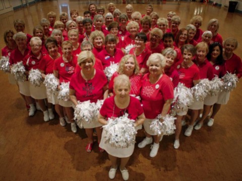 Photo of a cheerleader group composed of elderly women, all in red tops and white skirts, with pompoms