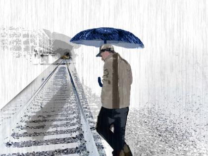 A man carrying an umbrella walks beside a set of train tracks