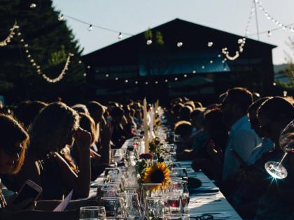 People gathered at a long, outdoor dining table set with wine glasses, candles, and flowers. 
