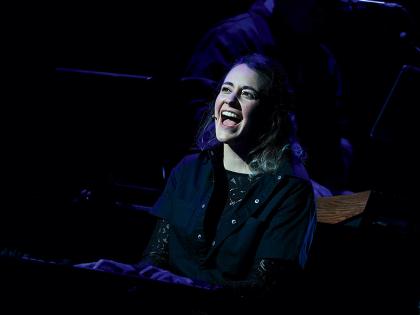 Madeline Benson singing at the piano, her face lit up on an otherwise dark stage