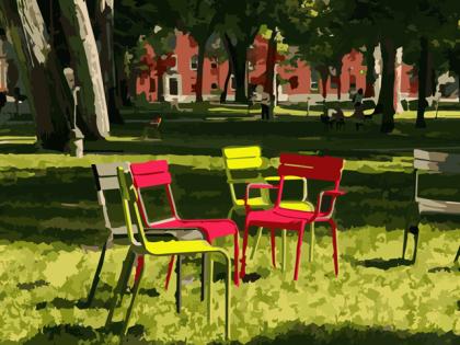 Colorful metal chairs arranged in a circle on the grass under trees in Harvard Yard. Red brick buildings in the background.