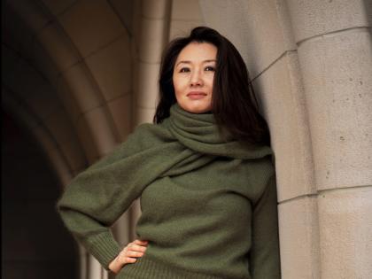 Portrait of Jeannie Suk Gersen, an elegantly dressed Korean American woman leaning against a stone archway.