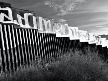 A photograph of the border wall stretching toward a mountain in the distance