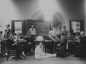 Several Harvard Computers and Radcliffe students pose for a photograph together, seated at desks and sitting on the floor