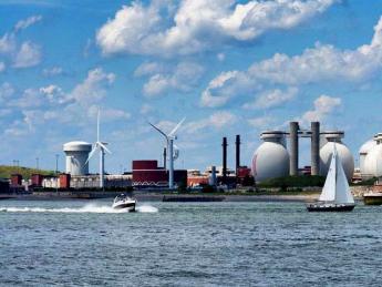 view from water of island holding giant steel eggs and wind turbines of wastewater treatment plant