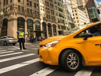 A yellow cab turns through an intersection directed by a police officer