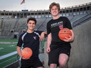 Two students pose in Harvard Stadium. One holds a basketball and the other holds a soccer ball.