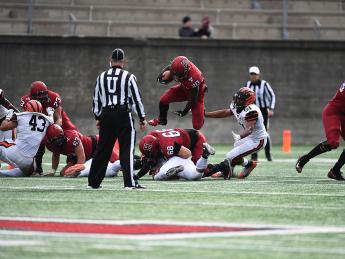 Harvard running back Aaron Shampklin hops over a Harvard teammate with a football in hand.