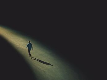 Drawing of a distant solitary figure walking alone toward the horizon along a narrowing path of light edged on both sides by darkness