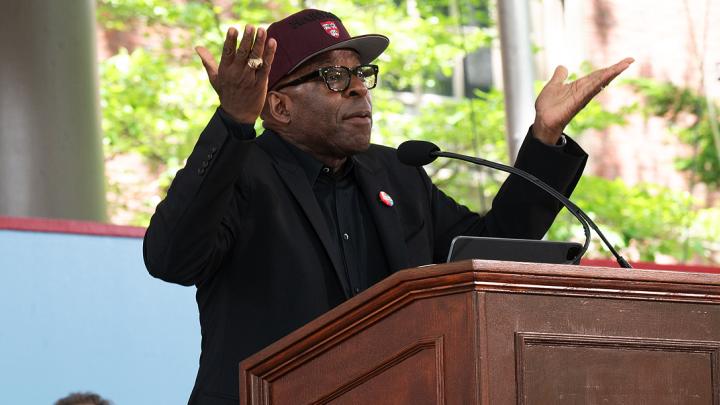 Man wearing red Harvard baseball cap addresses audience form podium