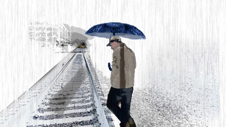 A man carrying an umbrella walks beside a set of train tracks