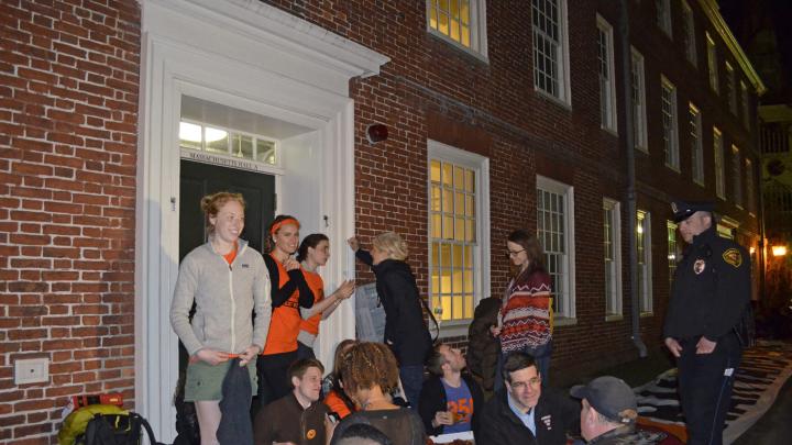 Students sit in front of an entryway to Mass. Hall, as Harvard University police look on.