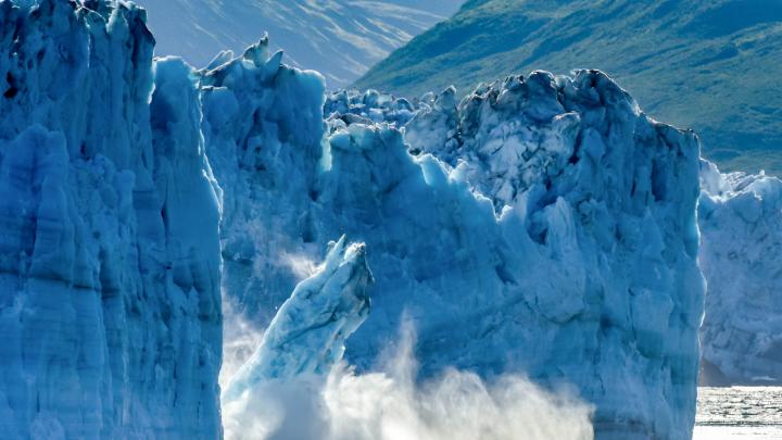 A photograph of a glacier breaking apart in Alaska, with large chunks of ice falling into the ocean.