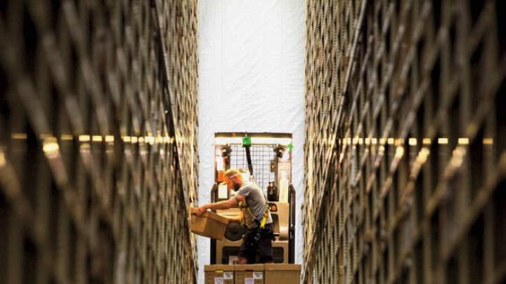 Photograph of worker between two enormously high stacked bookshelves at the Harvard Depository